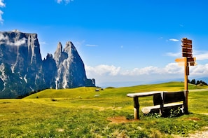 Un banc avec un panneau indicateur, situé dans un champ herbeux, avec des montagnes en arrière-plan.