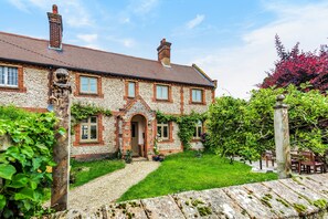 Une maison en pierre avec une façade en briques, une entrée centrale et un jardin bien entretenu agrémenté d’un patio.