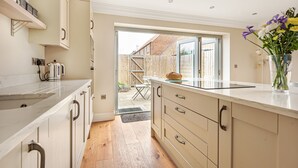 A modern kitchen with light wood cabinets, a marble countertop, and a view of the backyard through an open door.