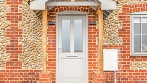 A white door with a stone and brick facade, a small porch, and a window to the right.