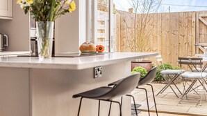 A modern kitchen with a central island, bar stools, and a wooden fence in the background.