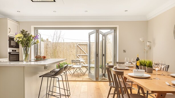 A modern kitchen with a central island, bar stools, and a dining area with a wooden table and chairs.