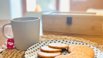 Una taza blanca con una bolsita de té, un plato con galletas y una alfombrilla tejida sobre una mesa.