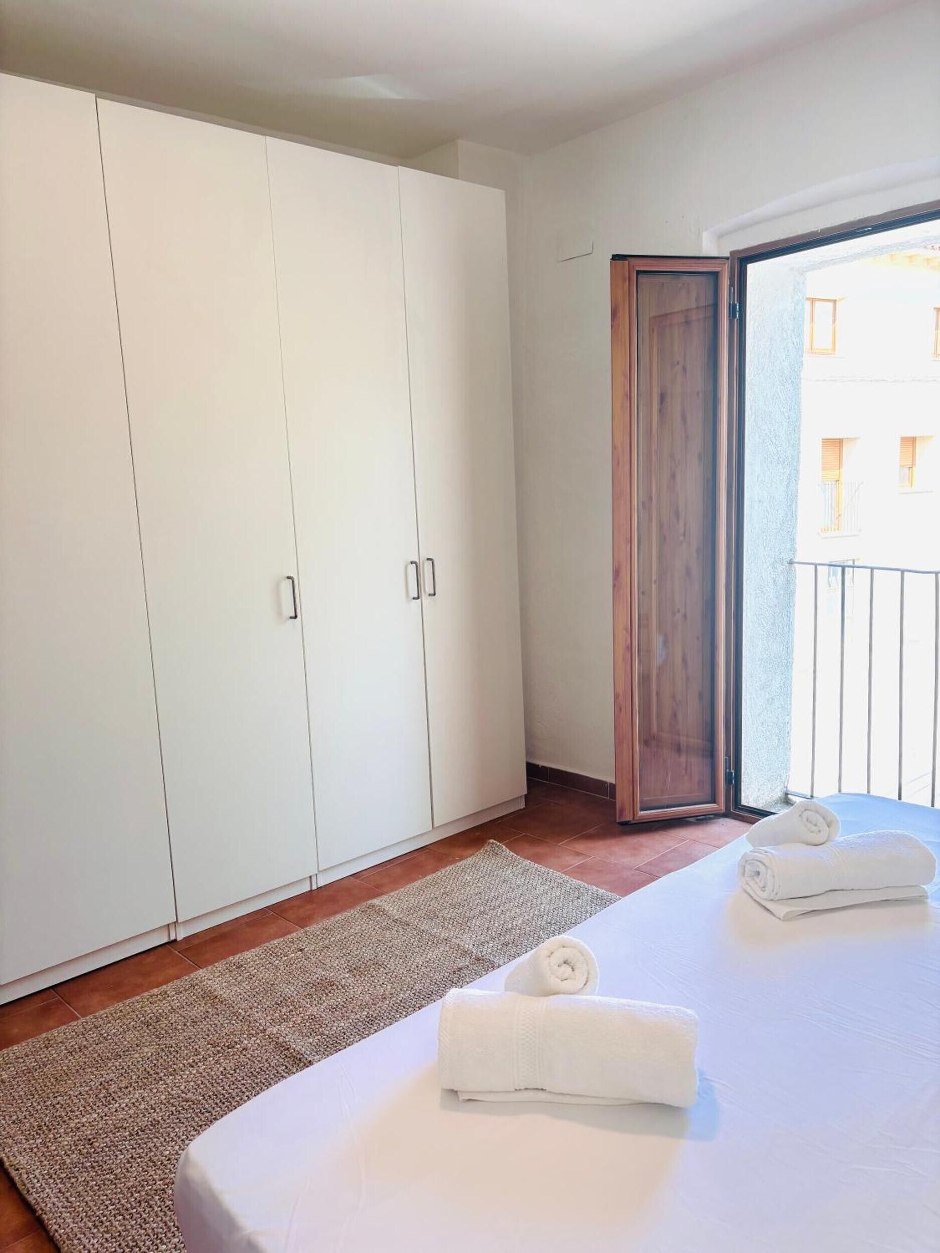 Habitación de hotel con un armario grande, una cama con dos toallas enrolladas, suelo de madera y vistas a través de una puerta abierta.