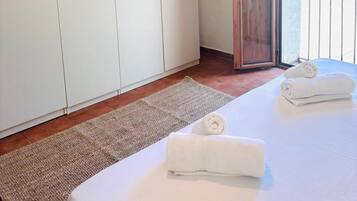 Habitación de hotel con un armario grande, una cama con dos toallas enrolladas, suelo de madera y vistas a través de una puerta abierta.