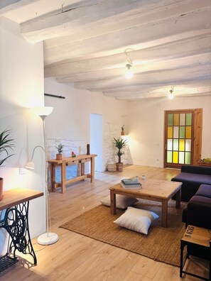 A cozy living room with a wooden coffee table, a sofa, a lamp, and a door with a colorful window. - Country-Style House in the Heart of Catalonia (Avinyó)