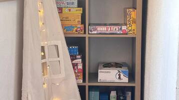 Une étagère remplie de divers jeux de société et un tissu blanc décoré de guirlandes lumineuses.