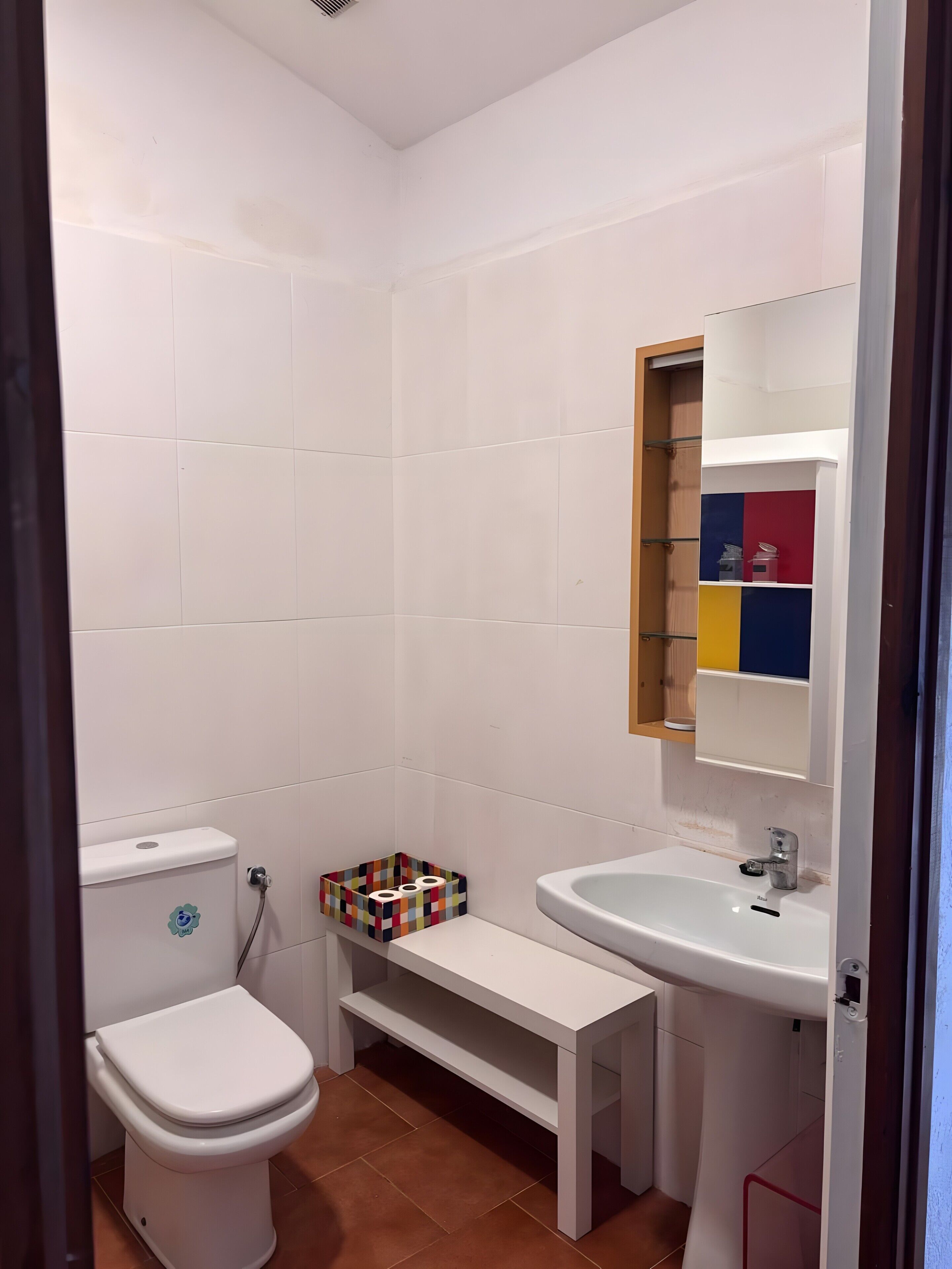 A bathroom with a toilet, sink, and a shelf with colorful storage boxes.