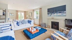 A living room with a white sofa, blue ottoman, and matching chairs, a fireplace, and a large painting of sailboats. - Sanderling - sleeps 7 guests  in 4 bedrooms (Burnham Market)
