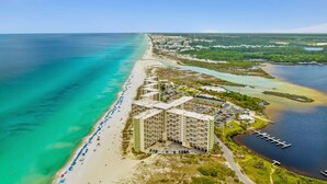 An aerial view of a coastal hotel with a beach, clear turquoise waters, and a marina.