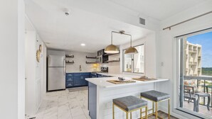 A modern kitchen with a central island, bar stools, and a large window offering a view of the city.