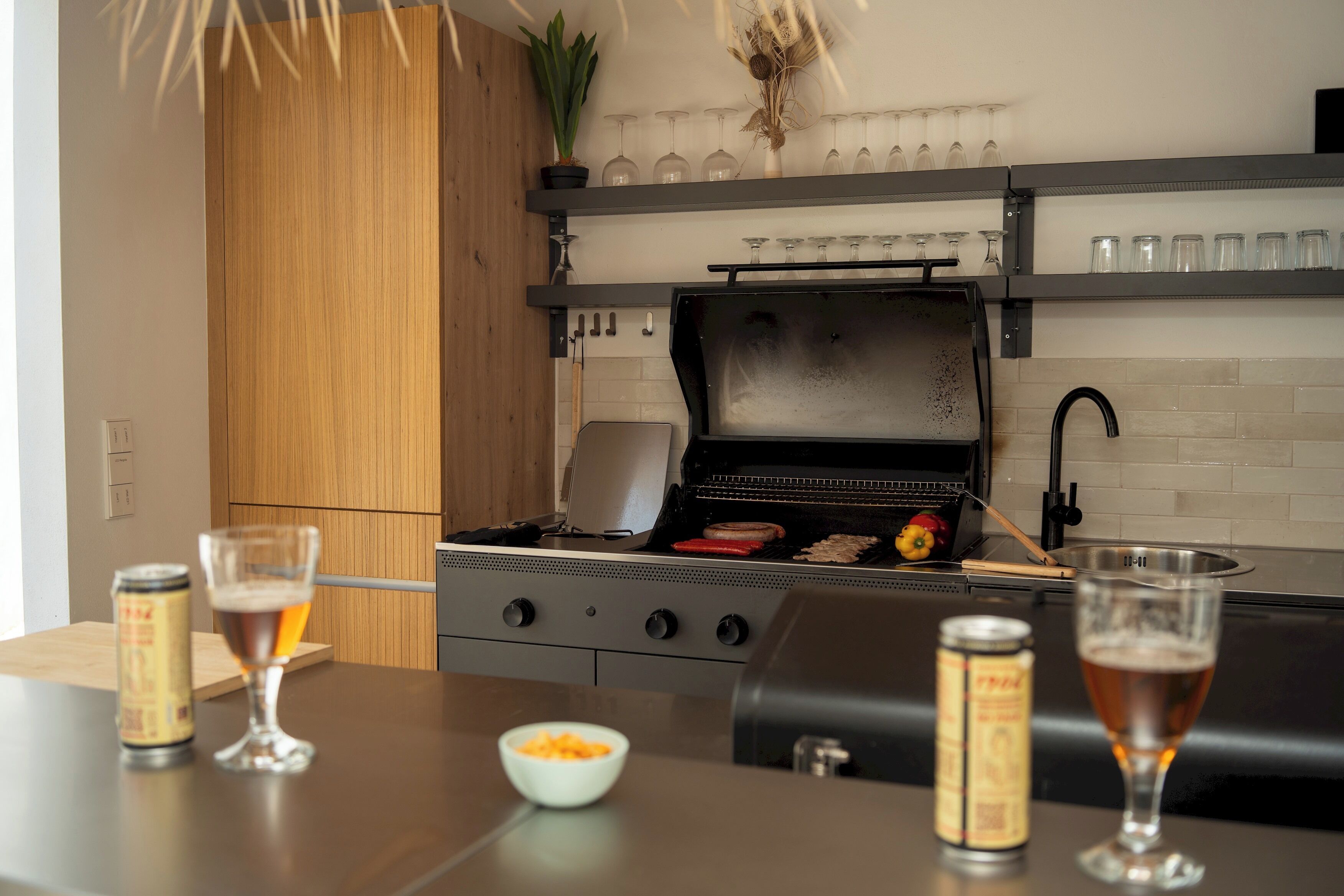 Eine Küche mit Grill, zwei Biergläsern, einer Schüssel Snacks und einem Blumentopf.