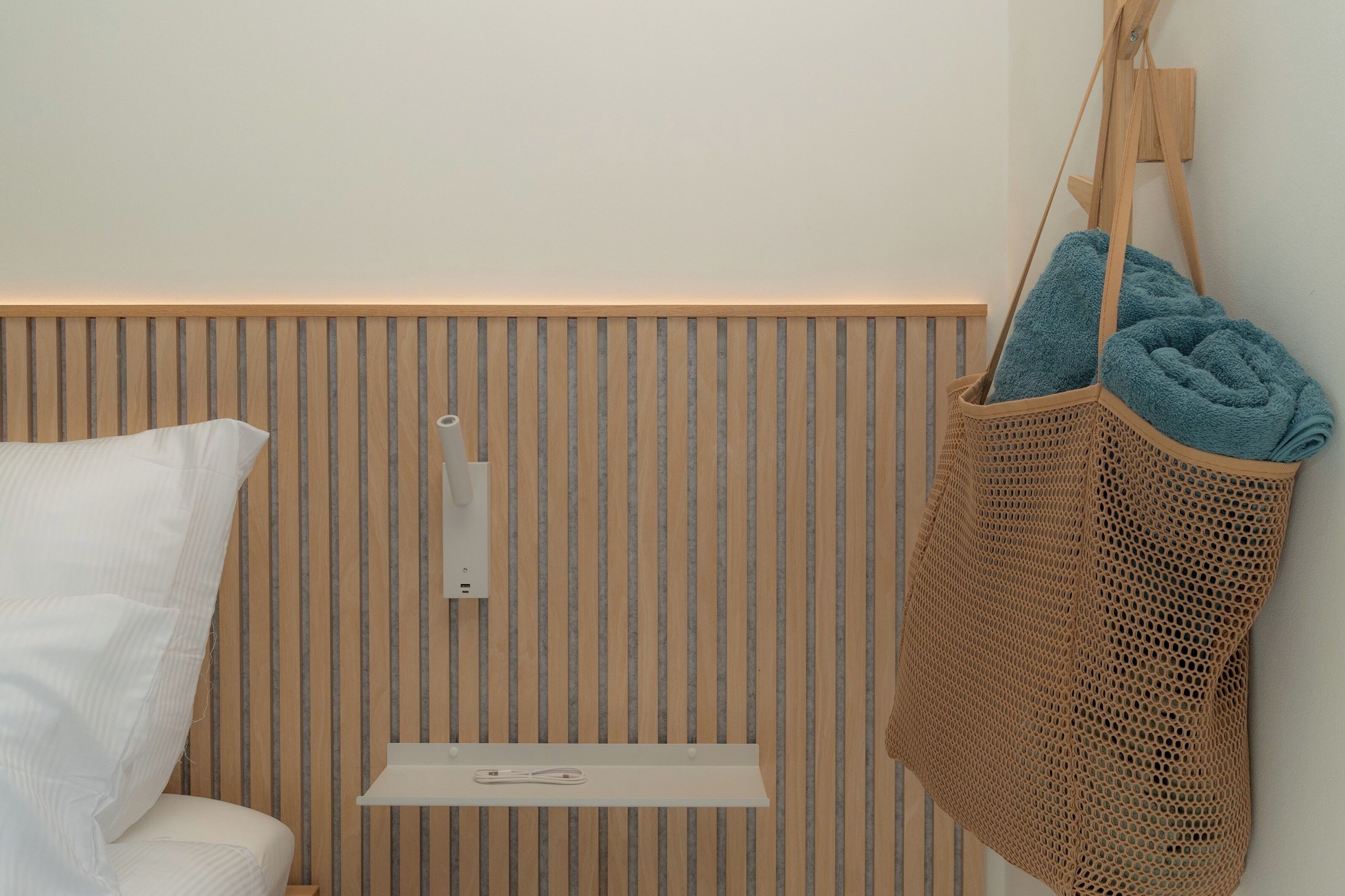 A bathroom with a wooden slat wall, a white shelf with a towel, and a hanging towel bag.