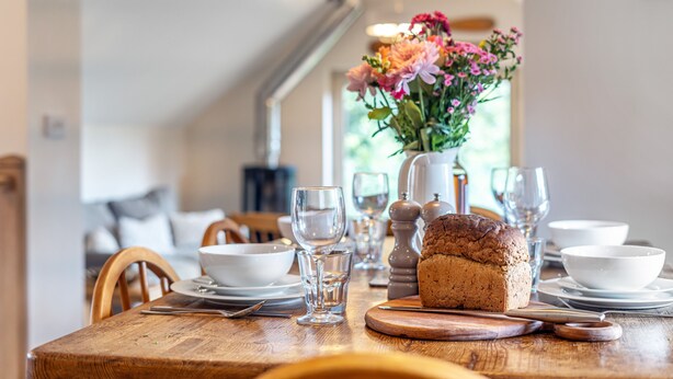 A wooden dining table with a loaf of bread, white bowls, and clear glasses. - Mill View Burnham Norton - sleeps 4 guests  in 2 bedrooms (Burnham Norton)
