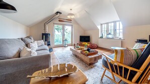 A spacious living room with a high ceiling, a large window, a sofa, a coffee table, and a TV. - Mill View Burnham Norton - sleeps 4 guests  in 2 bedrooms (Burnham Norton)