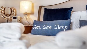 A neatly made bed with a pillow that reads "Sun, Sea, Sleep" and a bedside lamp. - Mill View Burnham Norton - sleeps 4 guests  in 2 bedrooms (Burnham Norton)