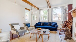 A living room with a blue sofa, grey armchairs, a wooden rocking chair, and a dog. - Edinburgh House - sleeps 8 guests  in 4 bedrooms (Burnham Market)