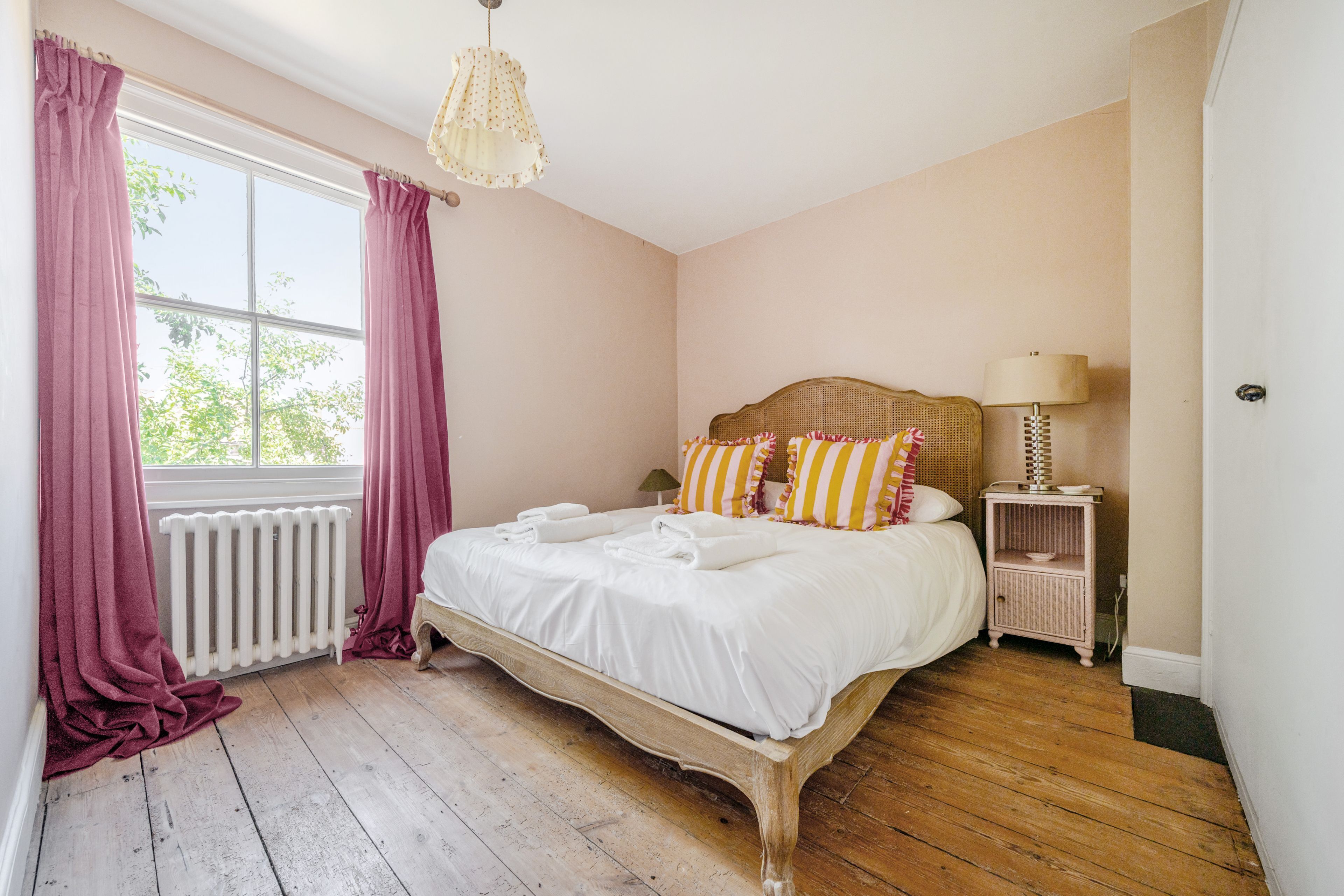 A bedroom with a wooden bed, a radiator, a nightstand, and a window with curtains.
