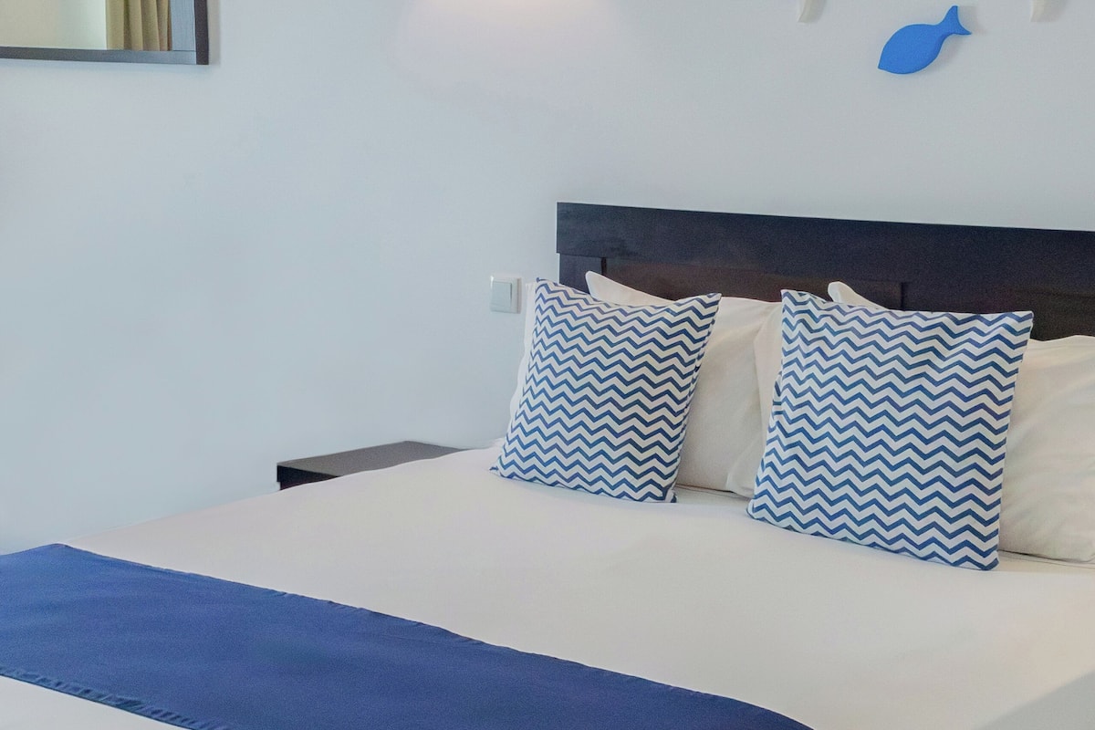 A hotel room with a bed, a nightstand, a wall-mounted light, and decorative fish wall art.