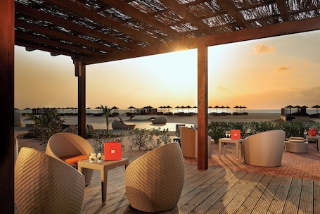 A beachside patio with wicker furniture, a laptop, and a sunset view.
