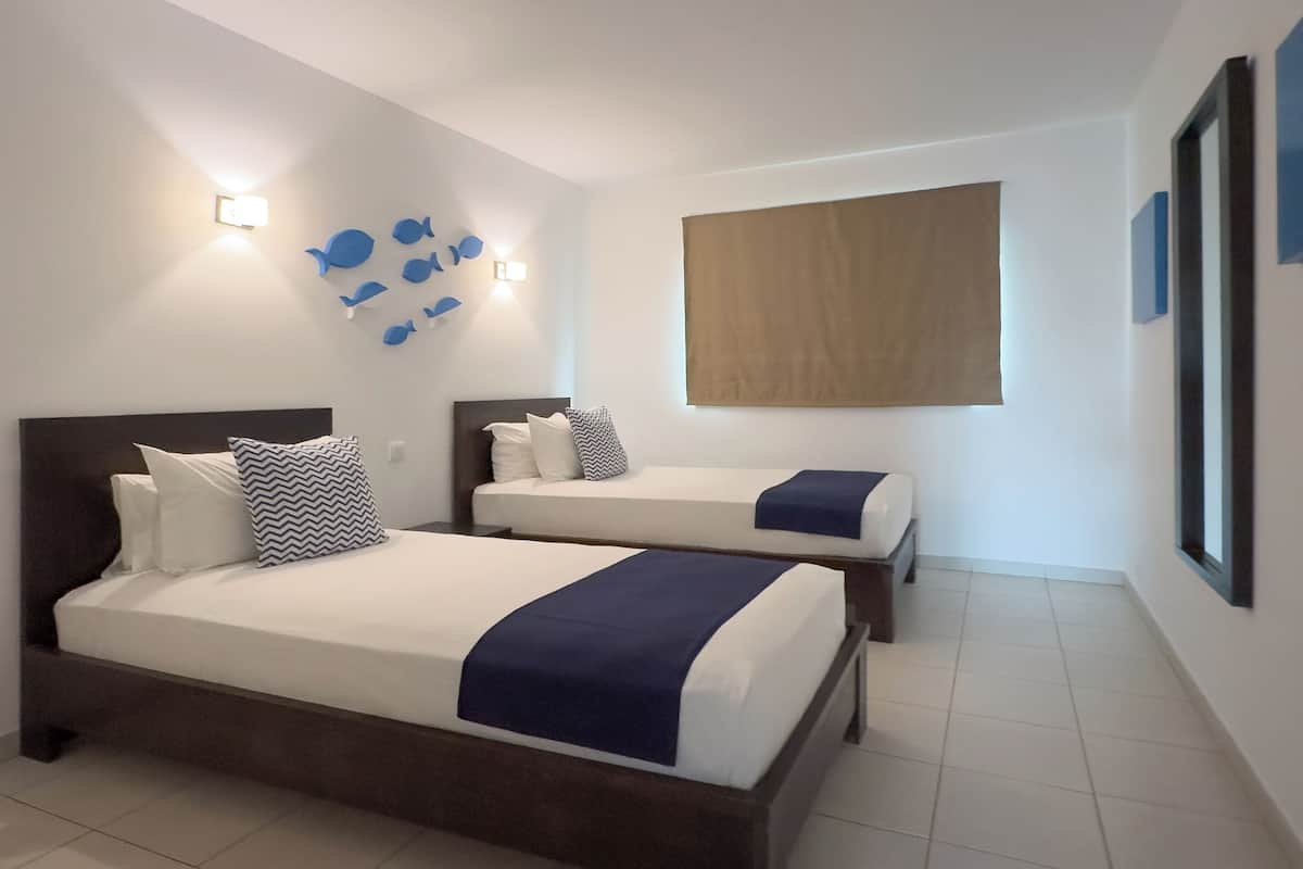 A hotel room with two beds, a wall-mounted light fixture, and a large window.