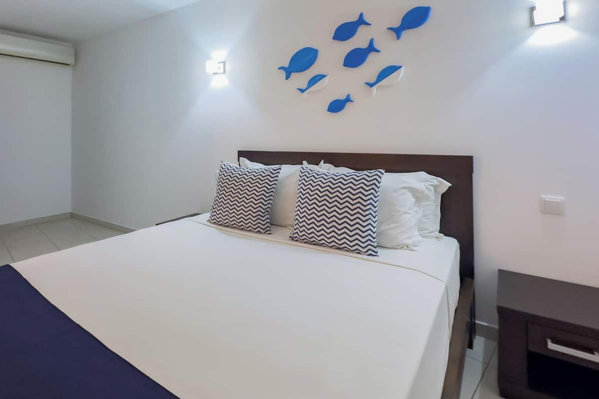A bedroom with a bed, two patterned pillows, a wall-mounted fish decoration, and a bedside table.