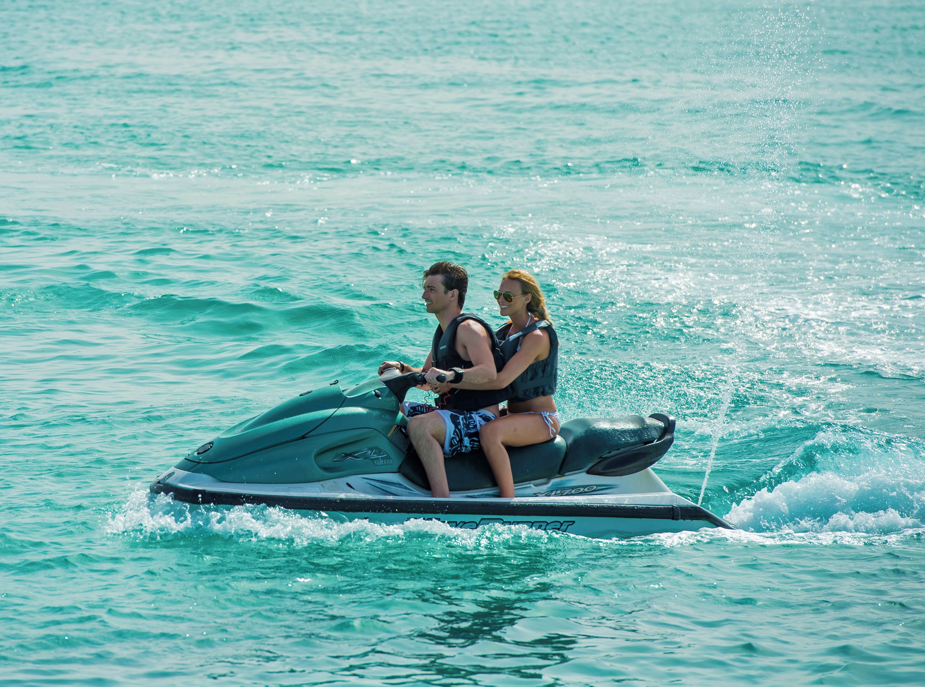 Dos personas en un jet ski sobre aguas turquesas.