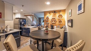 A modern kitchen with a central island, wooden wall decor, and a dining area with chairs. - Cozy 1-bedroom king condo w/fireplace in Snowshoe. Walk to slopes! (Snowshoe)