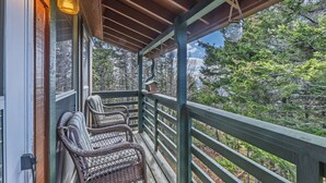 A wooden deck with wicker chairs, a railing, and a view of trees. - Cozy 1-bedroom king condo w/fireplace in Snowshoe. Walk to slopes! (Snowshoe)