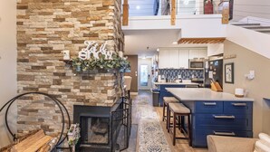 A modern kitchen with a stone fireplace, a bar area, and a view to the upper level. - Cozy 1-bedroom king condo w/fireplace in Snowshoe. Walk to slopes! (Snowshoe)