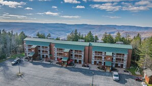 A multi-story hotel with a green roof, parking lot, and a view of mountains. - Cozy 1-bedroom king condo w/fireplace in Snowshoe. Walk to slopes! (Snowshoe)
