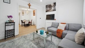 A modern living room with a grey sofa, a glass coffee table, and a dining area with a table and chairs.