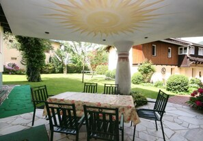 Eine Terrasse im Freien mit Tisch und Stühlen, einer Zierdecke und Blick auf einen Garten.