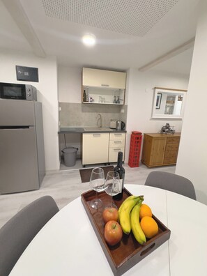 A modern kitchen with a microwave, refrigerator, and a dining table with a fruit tray.