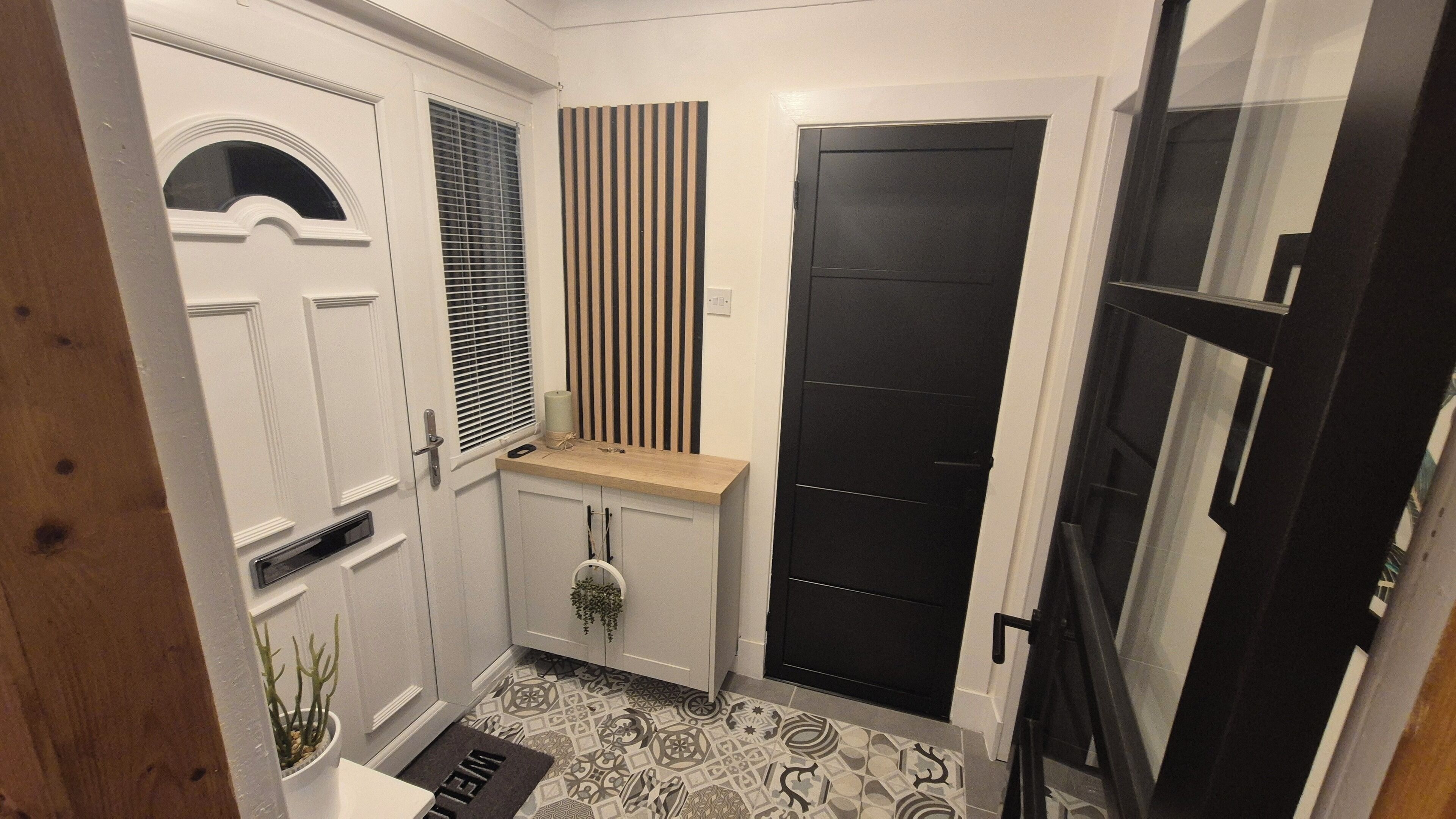 Un couloir avec une porte blanche, une porte noire et un banc en bois.