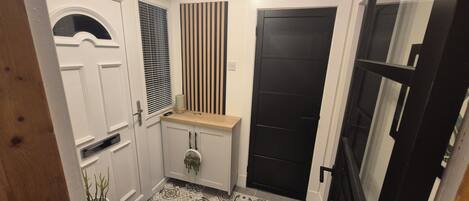 Un couloir avec une porte blanche, une porte noire et un banc en bois.