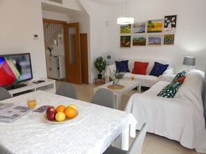 A living room with a dining table, a sofa, a TV, and artwork on the wall.