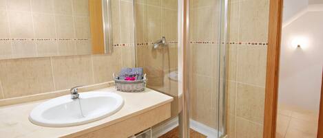 A bathroom with a sink, mirror, shower, and a basket with towels.