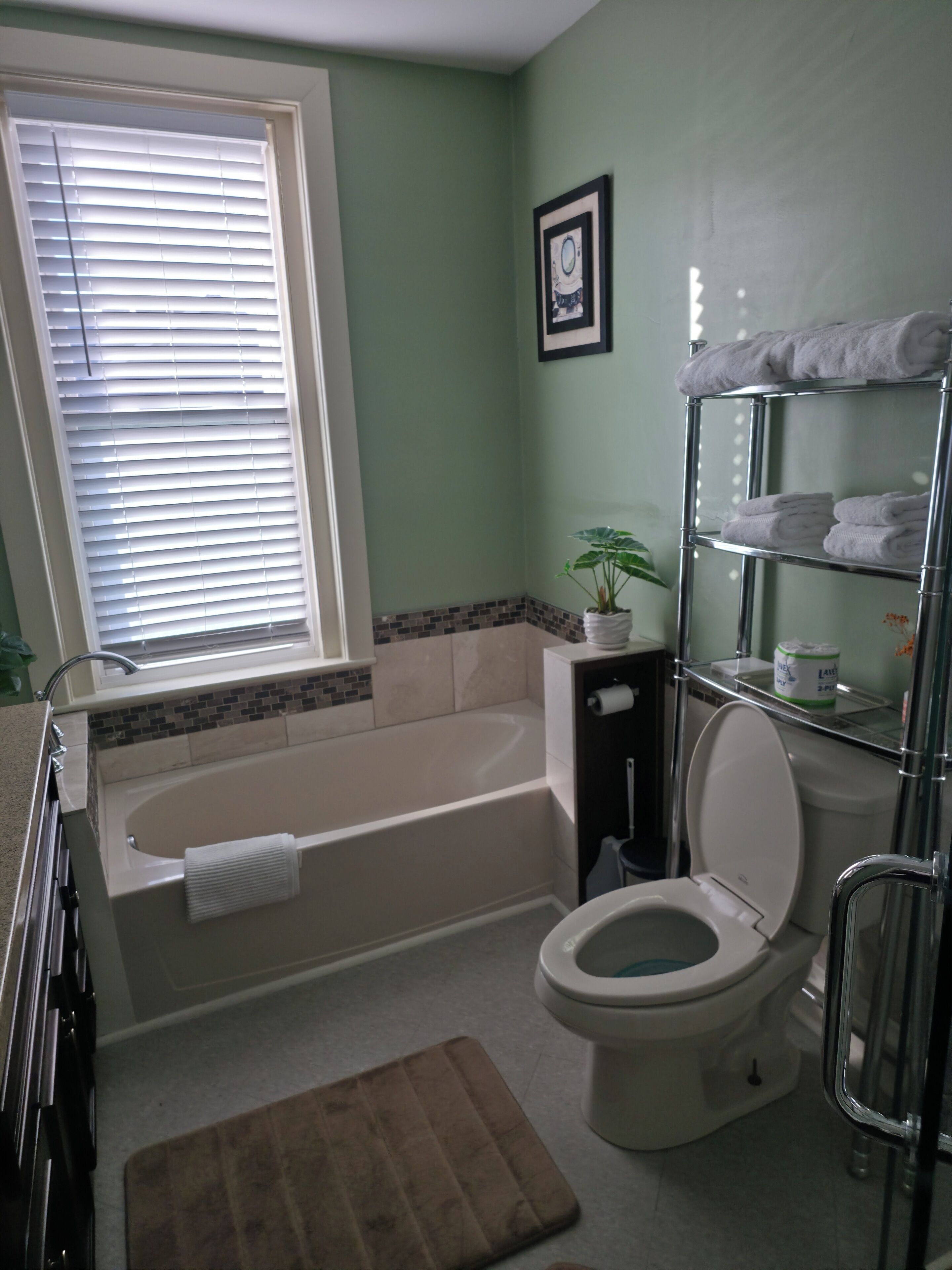 Ein Badezimmer mit Badewanne, Toilette und einem Fenster mit Jalousien.