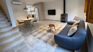 Un salon moderne avec un canapé, un coin repas avec des chaises, un téléviseur fixé au mur et une cheminée.