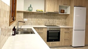 Une cuisine moderne dotée d’un plan de travail blanc, d’un évier en acier inoxydable, d’un four encastré et d’un réfrigérateur blanc.