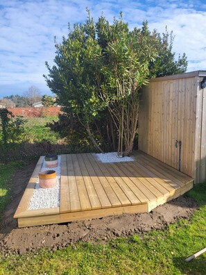 Una terraza de madera con un jardineras integradas y un pequeño cobertizo al fondo.