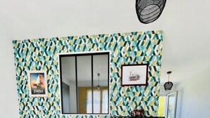 A living room with a patterned wall, a sofa, a coffee table, a side table, and a shelf with decorative items. - Vacation home at the gateway to Ile d'Oleron (Bourcefranc-le-Chapus)