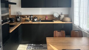 A modern kitchen with dark cabinetry, a wooden countertop, and a dining area with a table and chairs. - Vacation home at the gateway to Ile d'Oleron (Bourcefranc-le-Chapus)