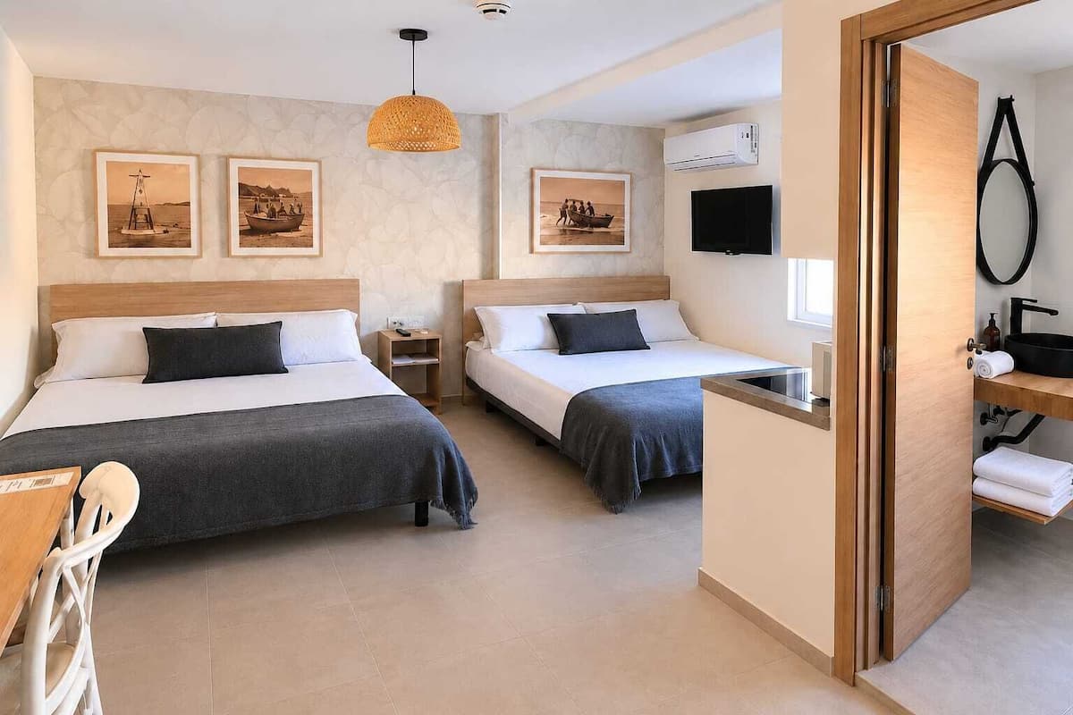 A hotel room with two beds, a TV, a bathroom with a mirror, and artwork on the walls.