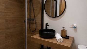 A modern bathroom with a glass shower enclosure, a wooden vanity, a round mirror, and a toilet.