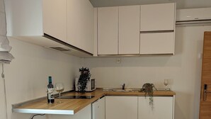 Eine kleine Küche mit weißen Schränken, einer Holz Arbeitsplatte, zwei Barhocker, einer Mikrowelle und einem Spülbecken.
