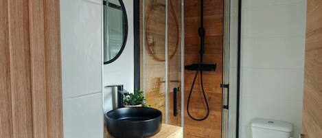A modern bathroom with a glass shower enclosure, a wooden vanity, a toilet, and a small potted plant.