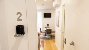Un couloir avec une porte portant le numéro « 2 », un interphone noir et, au fond, un coin repas.