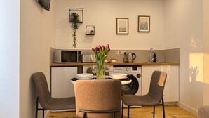 Une cuisine compacte dotée d’appareils électroménagers modernes, un coin repas avec deux chaises et une petite table agrémentée d’un vase de fleurs.